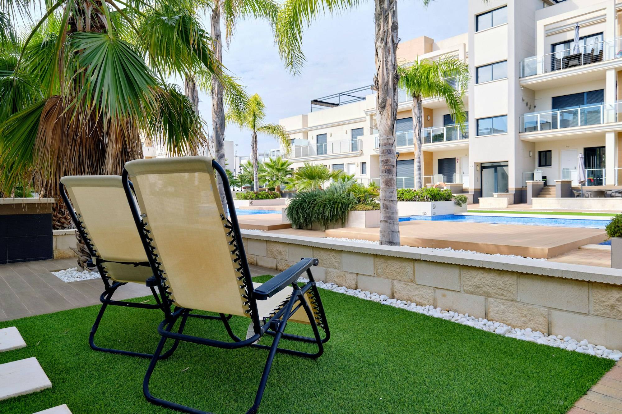 Two lounge chairs on the artificial grass overlooking modern apartments and swimming pools